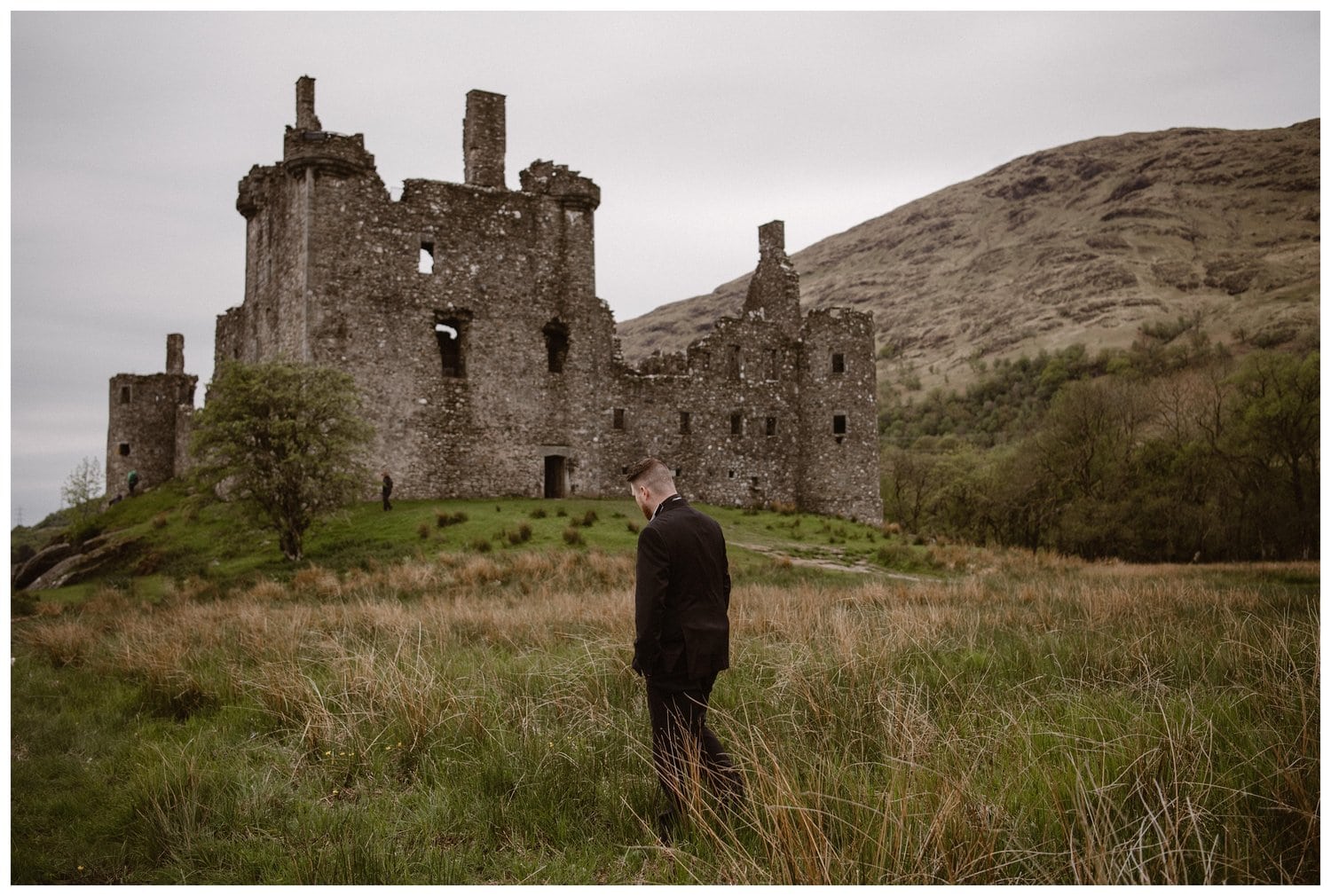 Groom standing in front of Kilchurn Castle in the Scottish Highlands. 