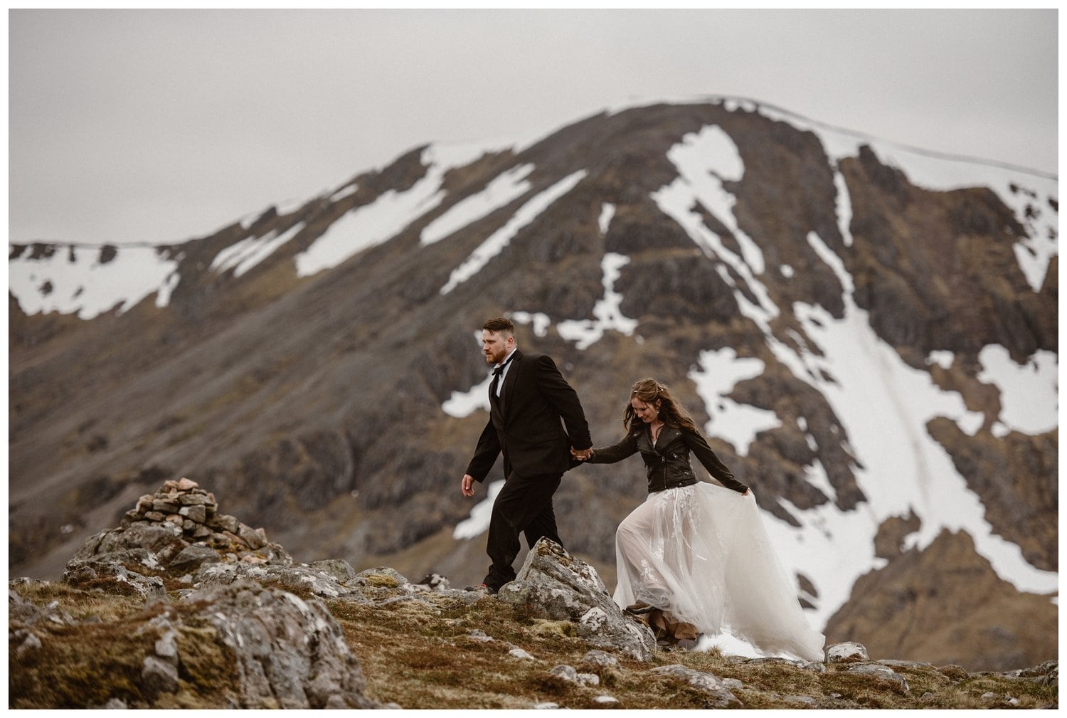 Bride and groom hold hands and walk through the Scottish Highlands on their elopement day. Glencoe Mountain is in the background. 