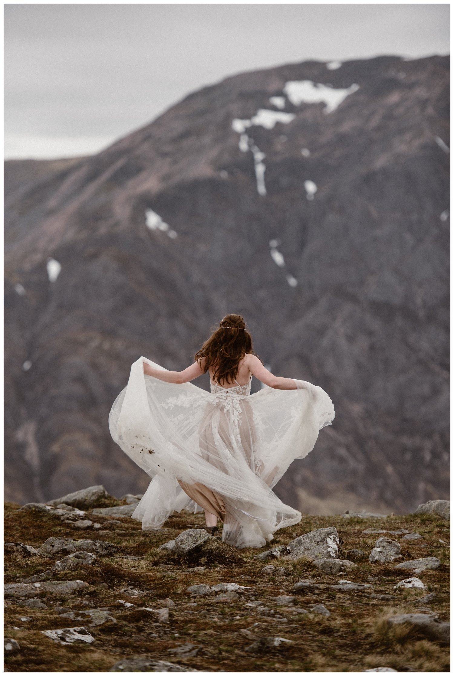 Bride walking through the Scottish Highlands while holding up the skirt of her white dress. 