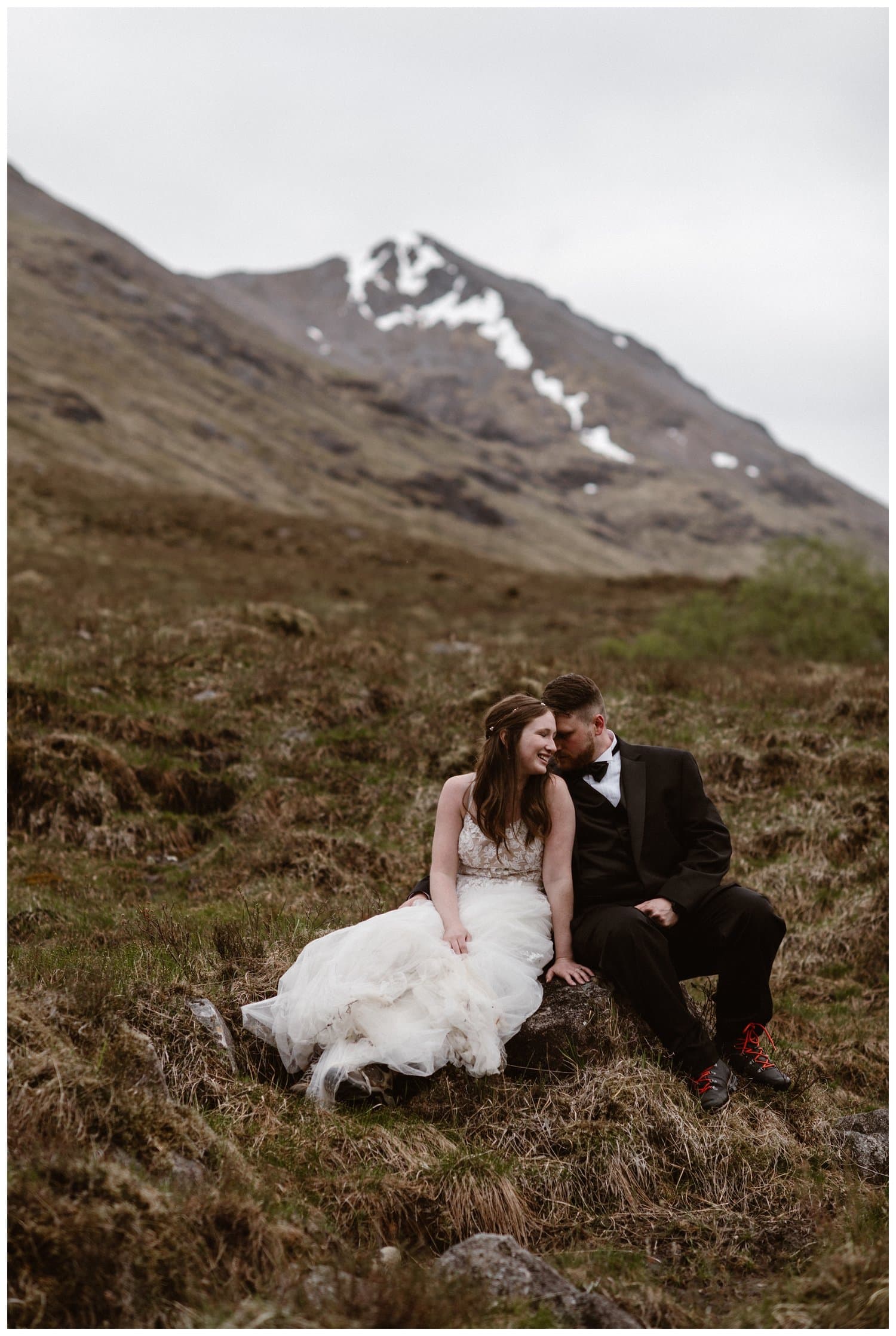 Bride and groom sit on a rock together on their elopement day in the Scottish Highlands. 