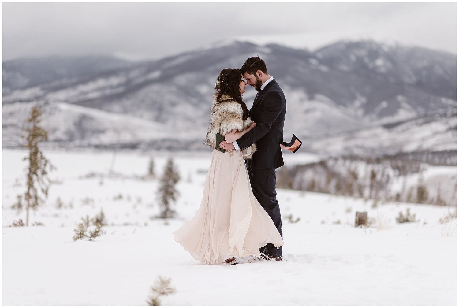 Bride and groom embrace during intimate elopement ceremony at Sapphire Point, Colorado. There is snow covering the ground and mountains in the background. 