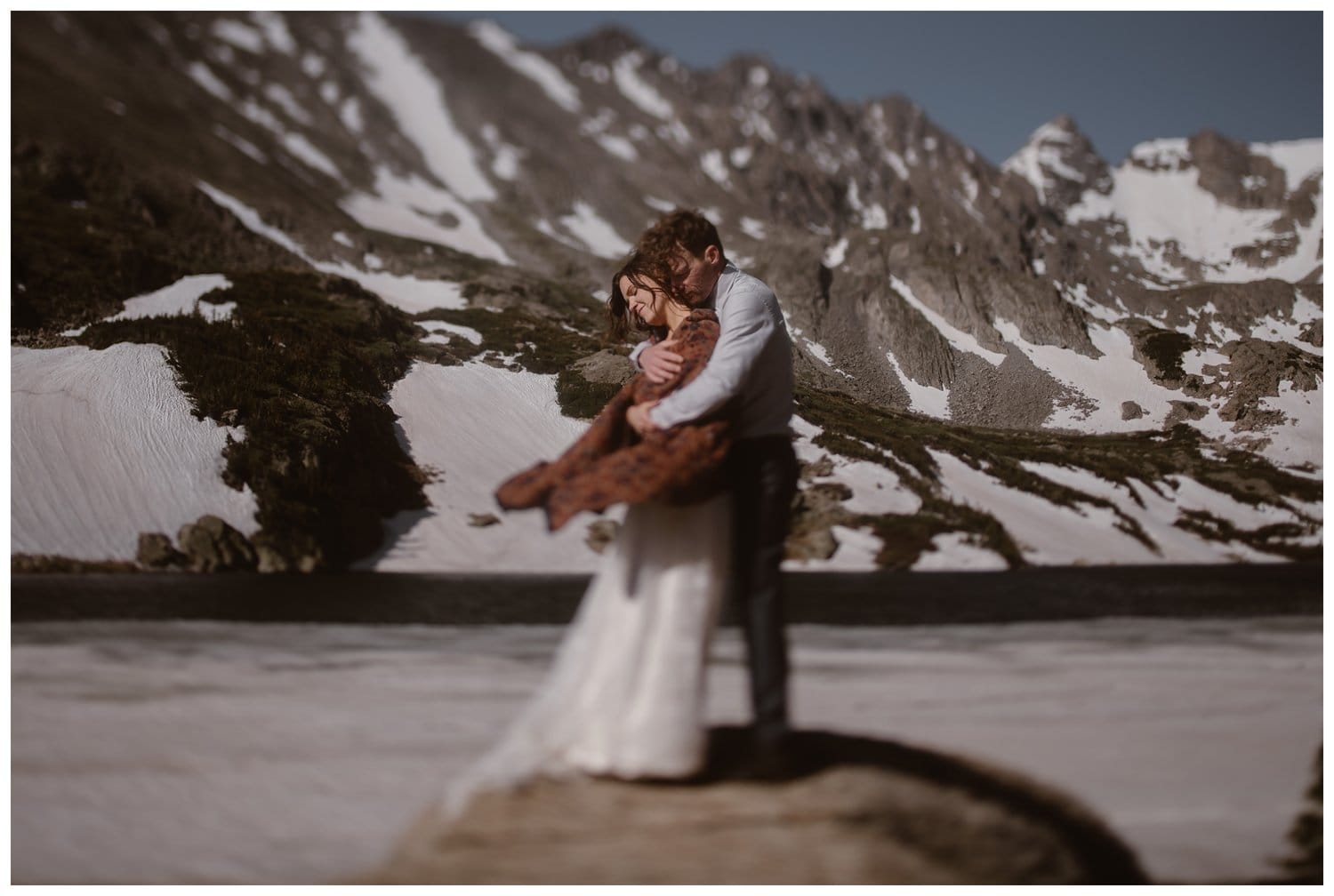 Bride and groom embrace in front of an alpine lake at the Indian Peaks, in Colorado. 