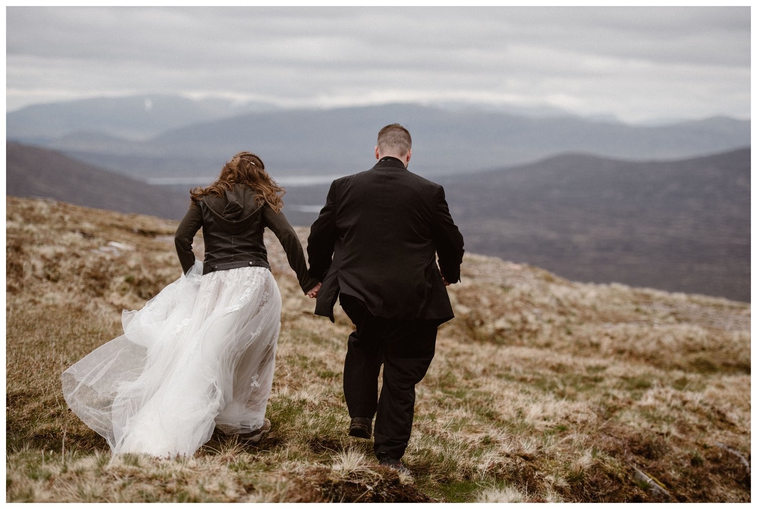 Bride and groom walk through the Scottish Highlands together while holding hands.