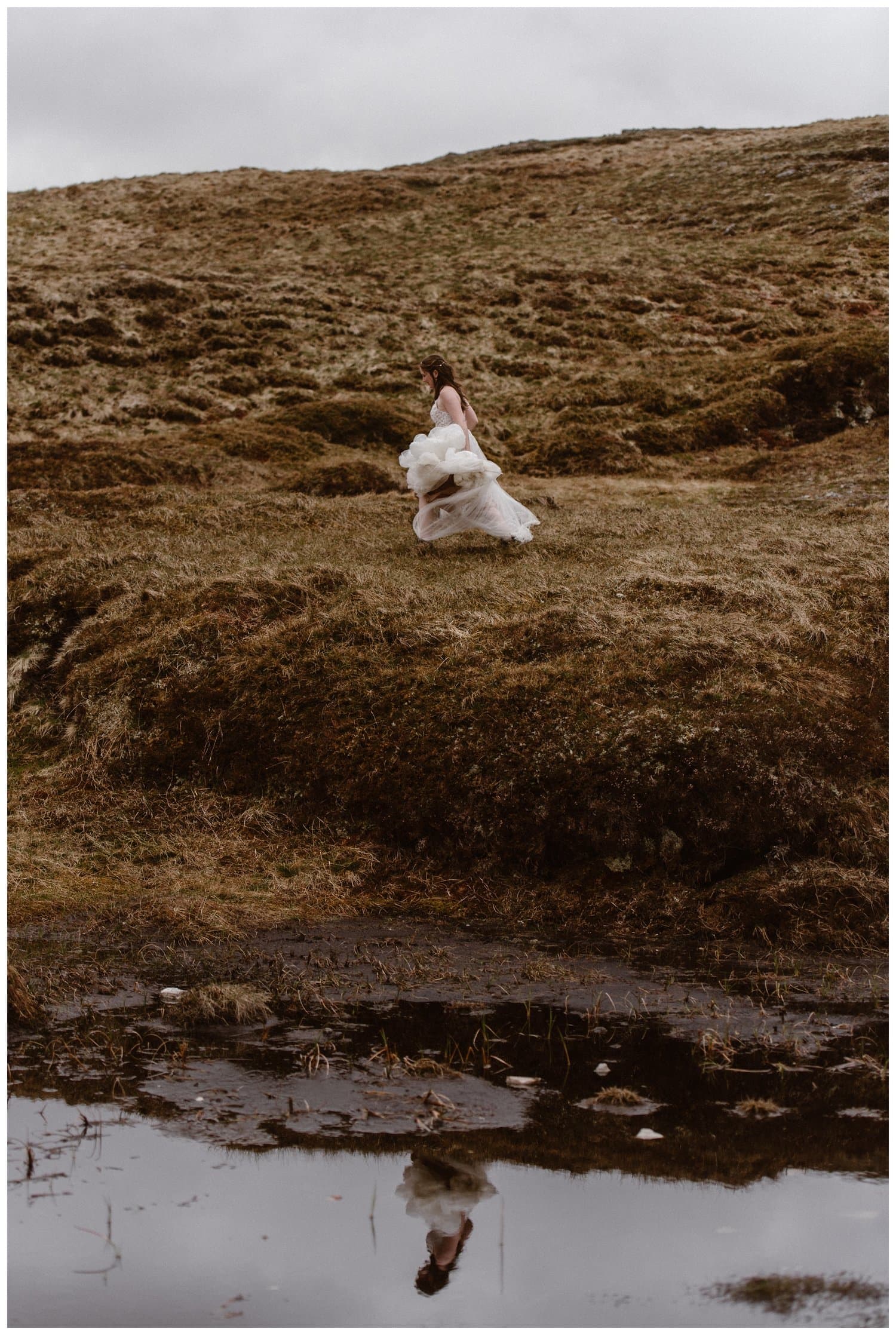 Bride running through the Scottish Highlands, wearing a white dress, which is flowing behind her. 