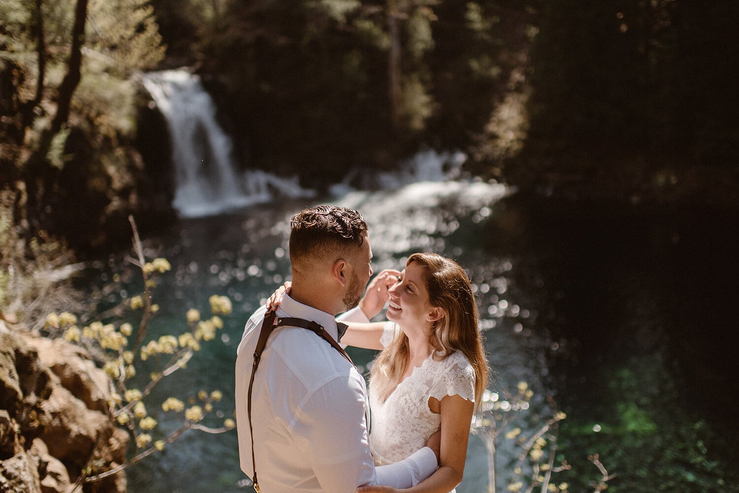 A bride and groom smile at each other while standing in front of an Oregon waterfall.