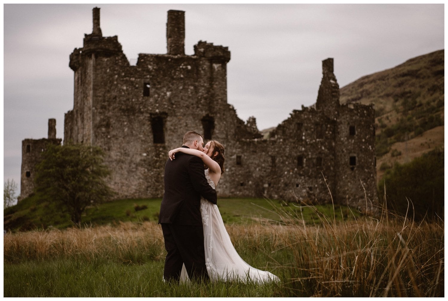Bride and groom share a kiss in front of Kilchurn Castle in the Scottish Highlands. 