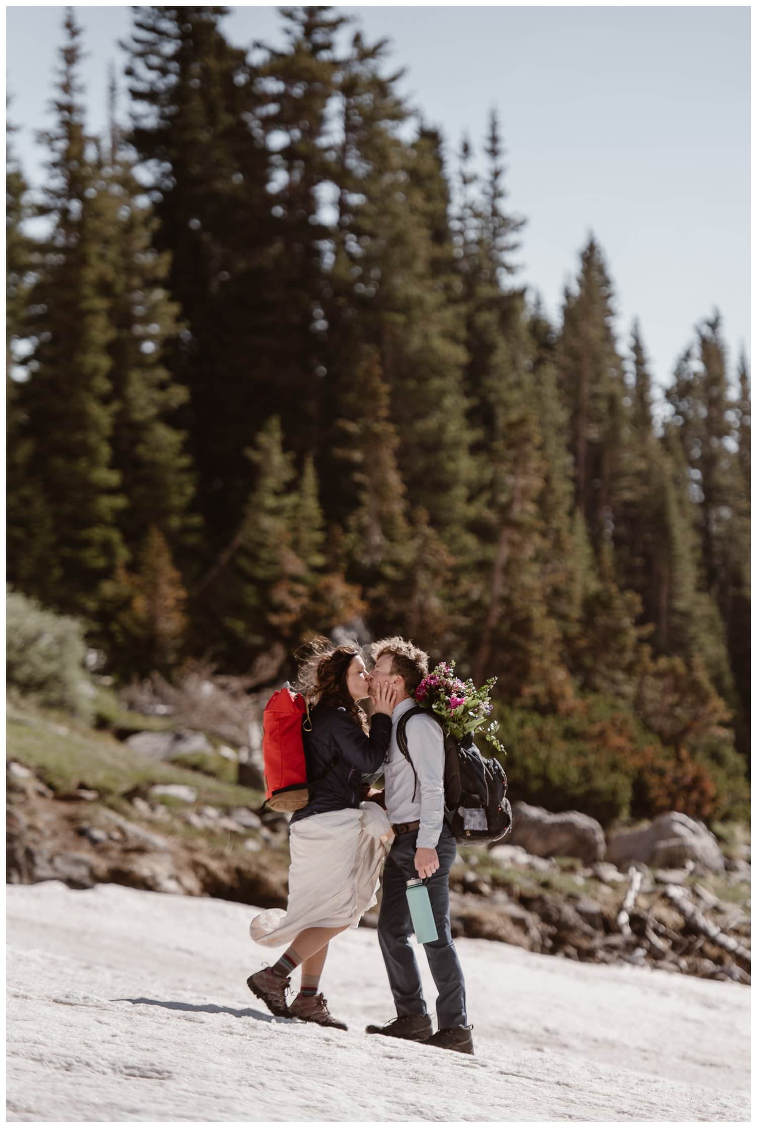 Bride and groom kiss while wearing their hiking backpacks, at the Indian Peaks in Colorado. 