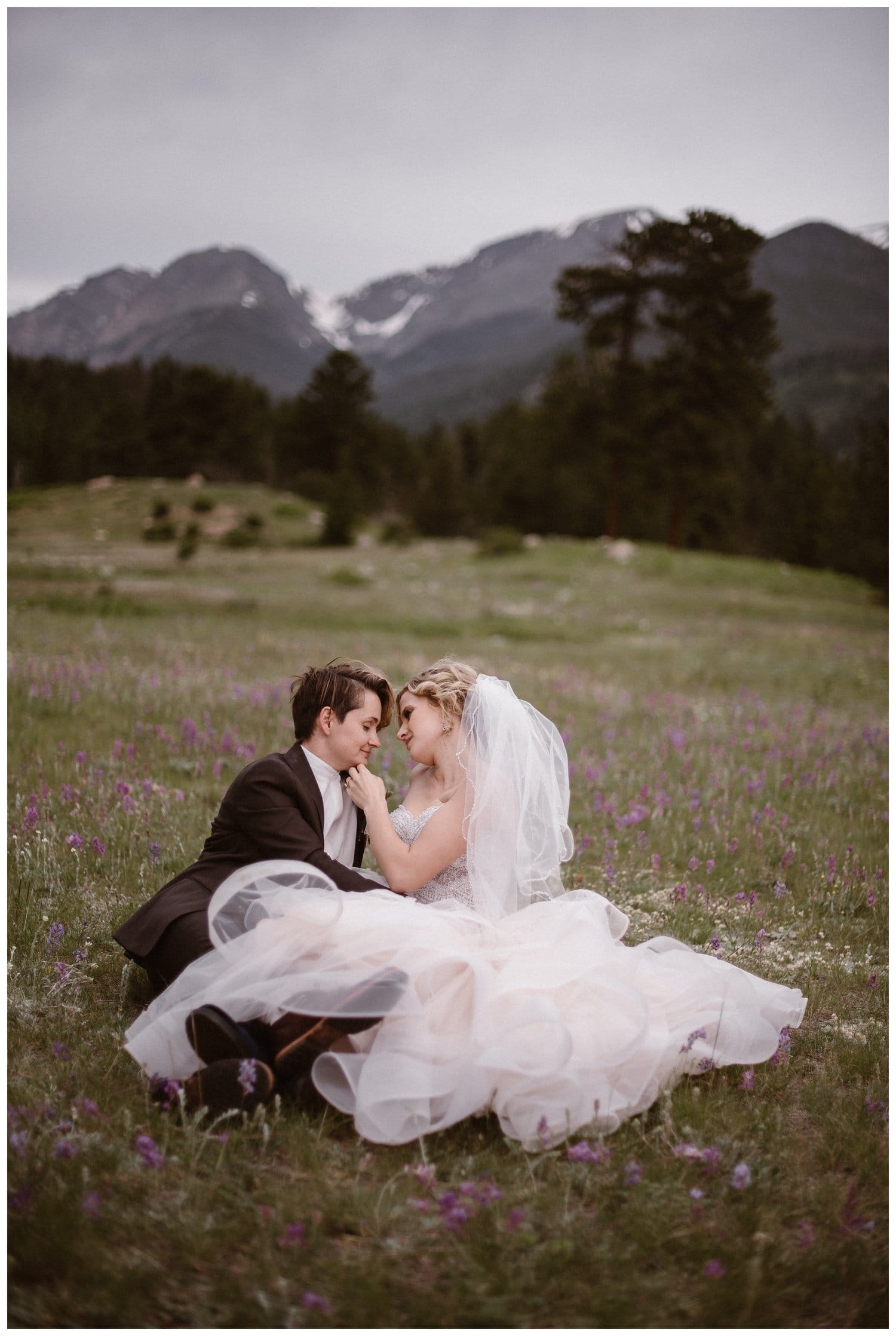 Two brides relaxing in a meadow of white and purple wildflowers in Rocky Mountain National Park, Colorado. 