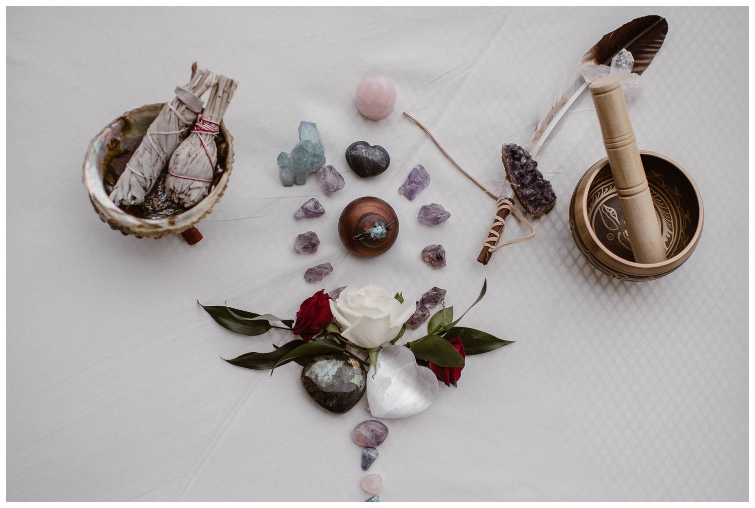 Crystals, sage, and roes arranged on a white cloth for reiki inspired ceremony in Colorado. 
