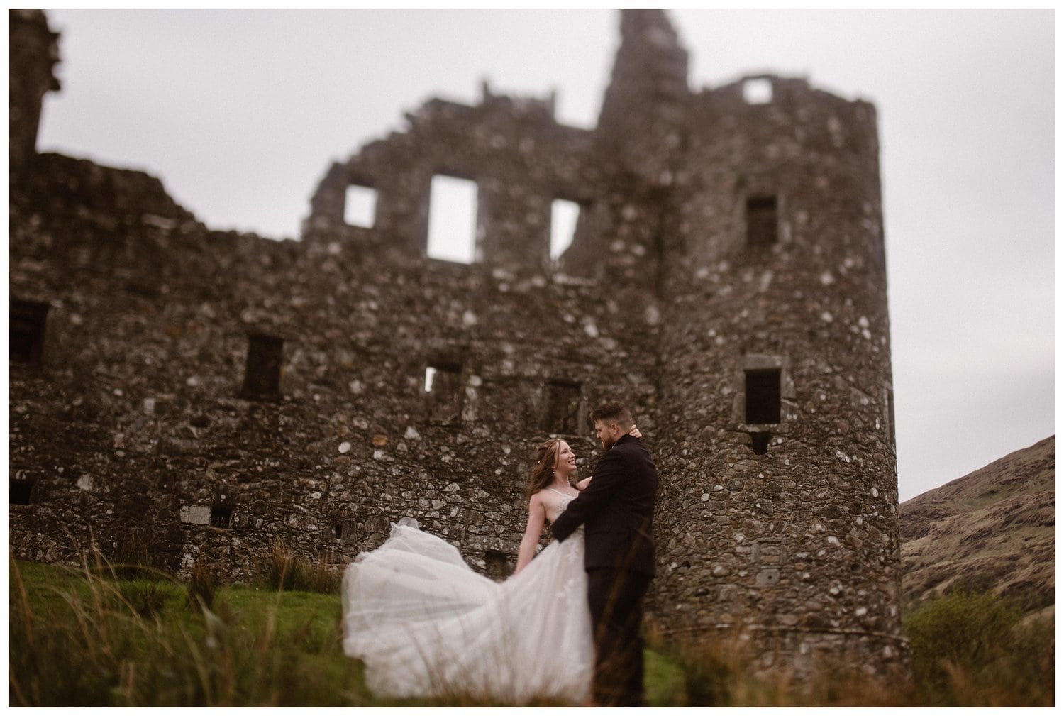 Bride and groom embrace in front of Kilchurn Castle in the Scottish Highlands. 