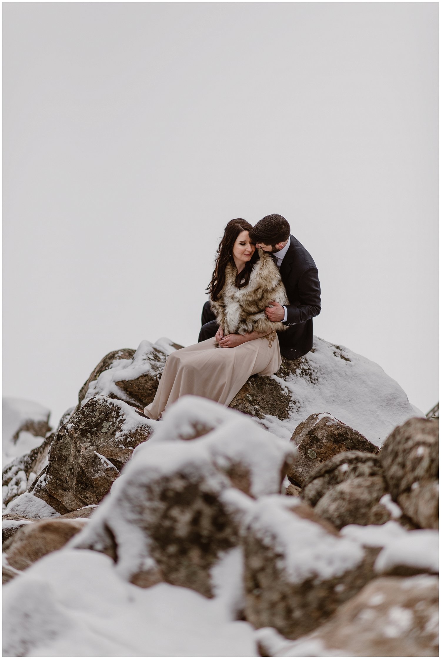 Bride and groom sitting on a rock together, surrounded by snow, at Sapphire Point, Colorado. 