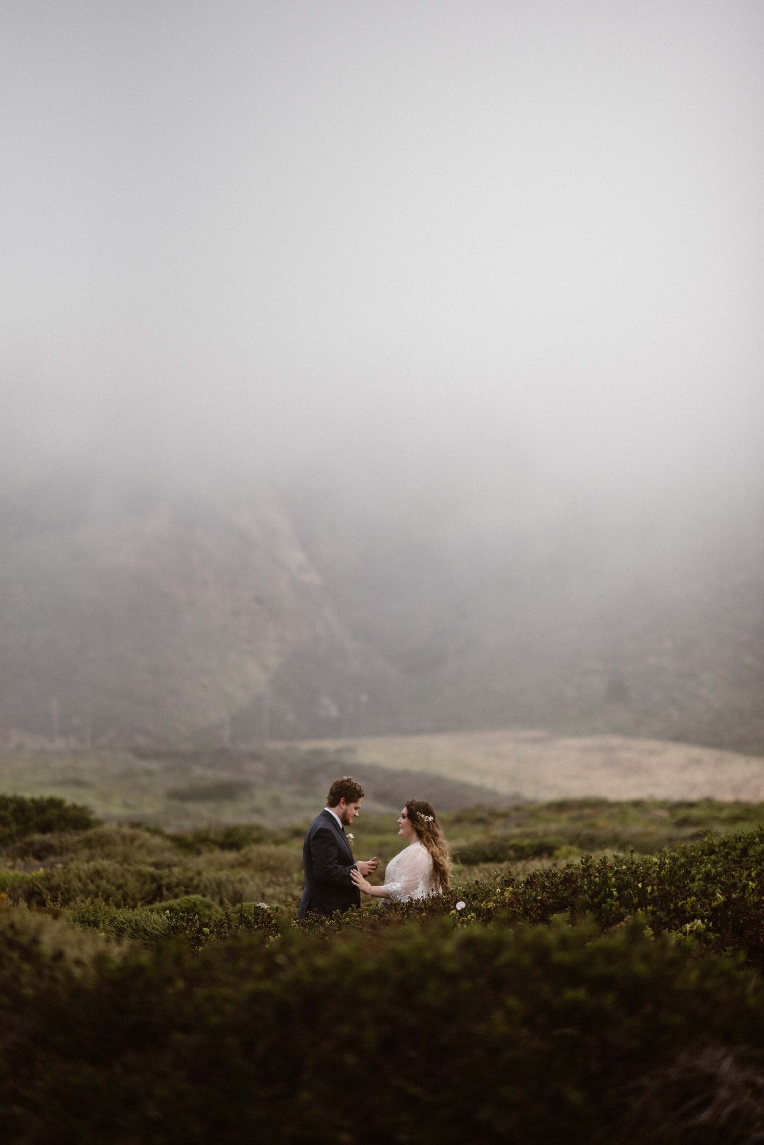 Groom reads his vows to bride and they are surrounded by waist-high  greenery in Big Sur, California.