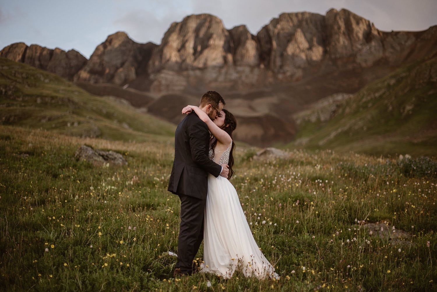 Bride and groom kiss, surrounded by a field of wildflowers in the San Juan Mountains. 