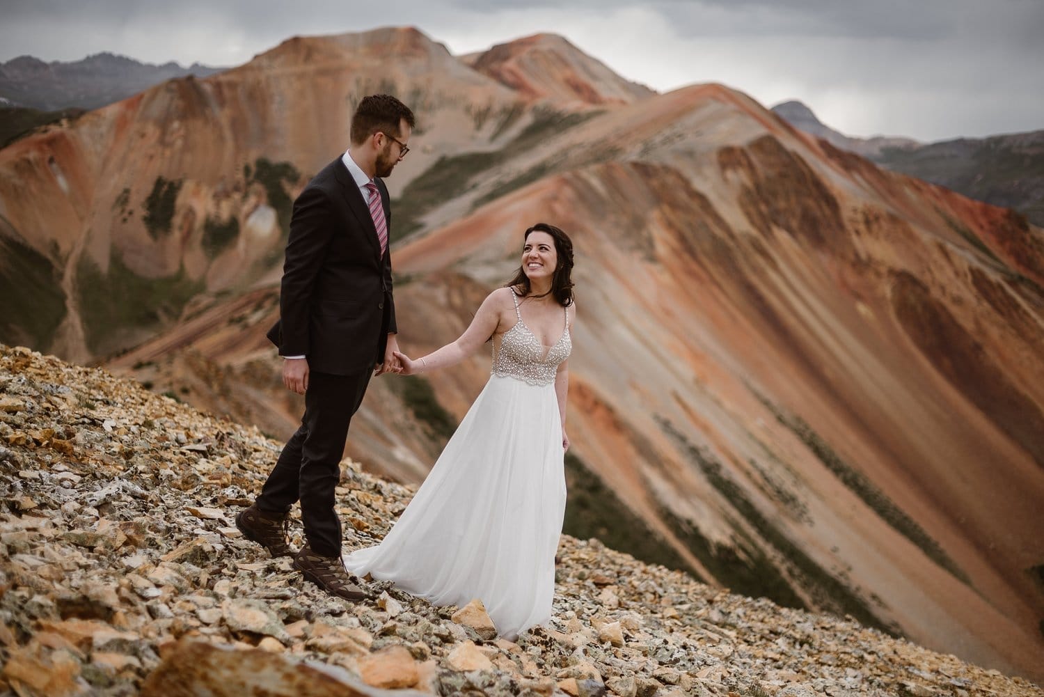 Bride and groom hold hands and walk along San Juan Mountains. 