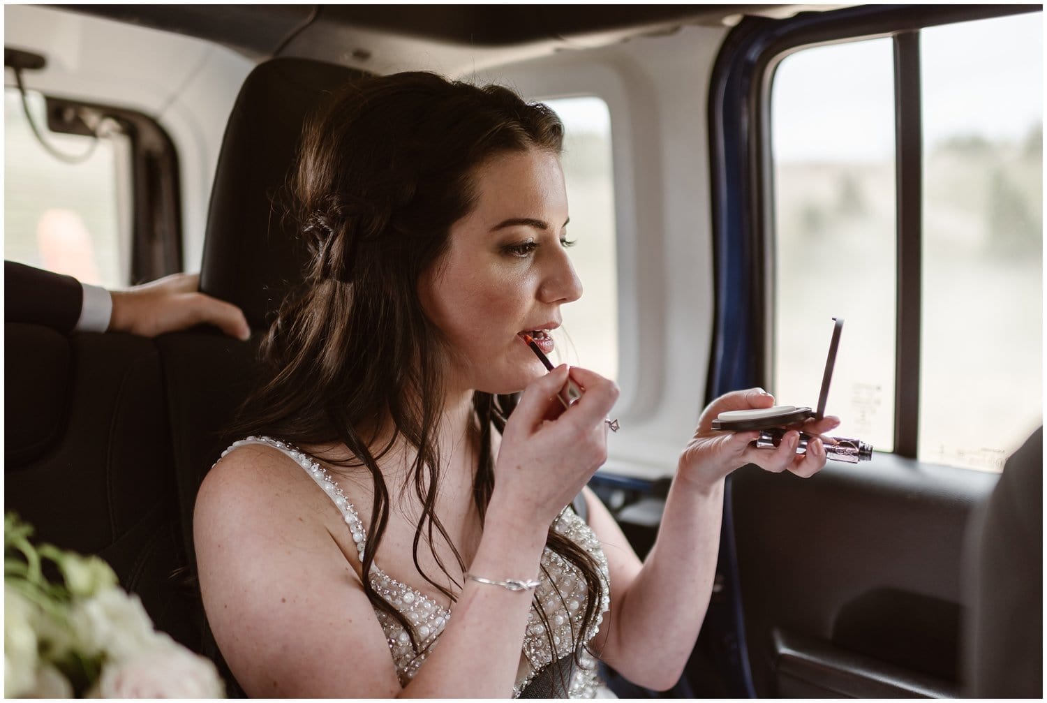 Bride applies lipgloss while looking into hand mirror and sitting inside Jeep.