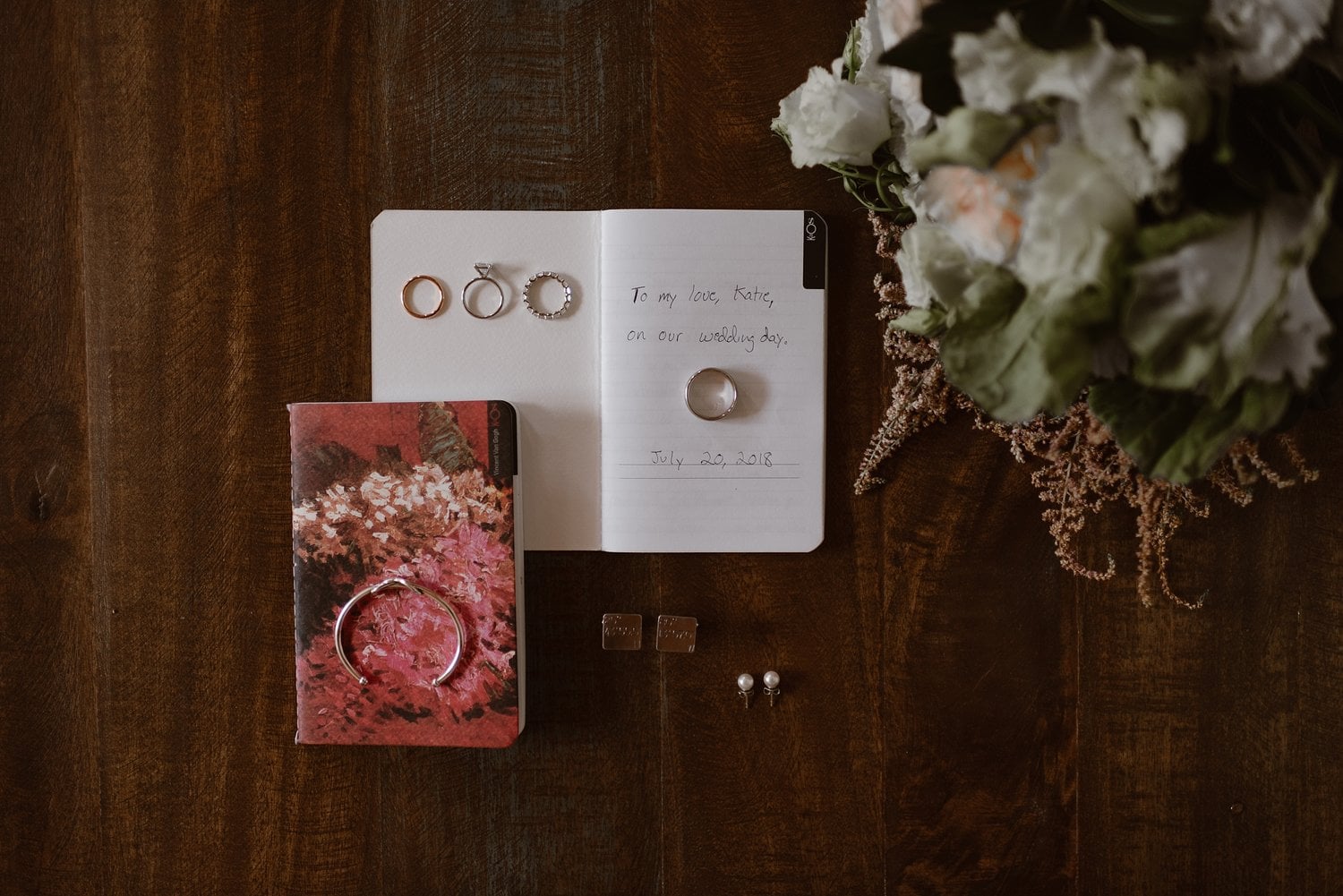 Flat lay of vow books, rings, and flowers. 