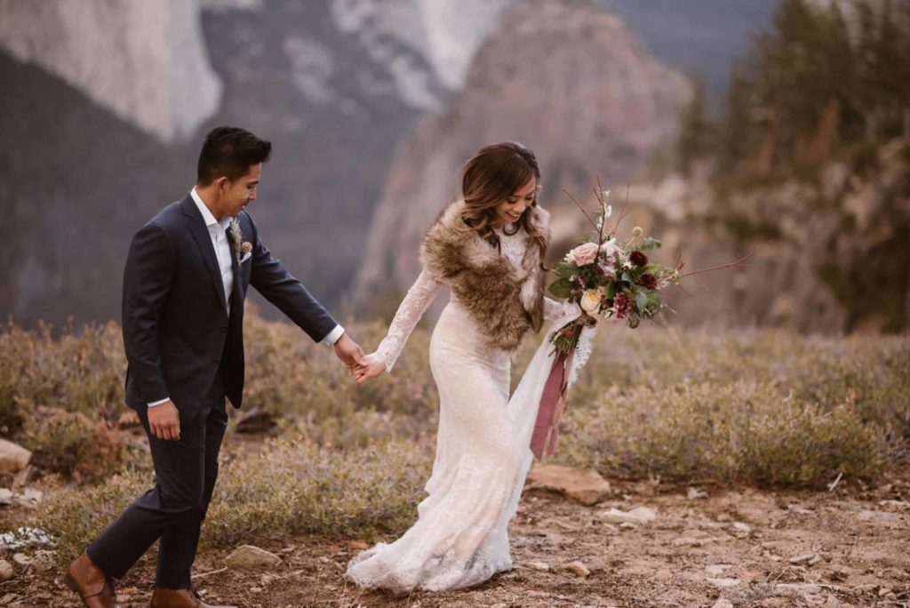 Bride and groom hold hands while walking in Yosemite National Park. 