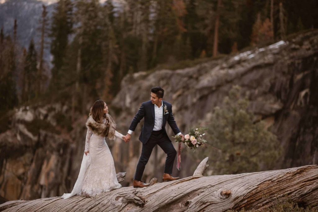 Bride and groom walk along a fallen tree, while holding hands in Yosemite National Park.