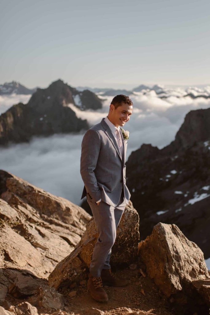 Groom smiling with hands in his pocket. Fog and mountains in the background. 