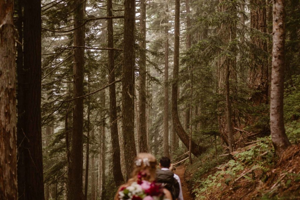 Bride and groom hiking through forest. 