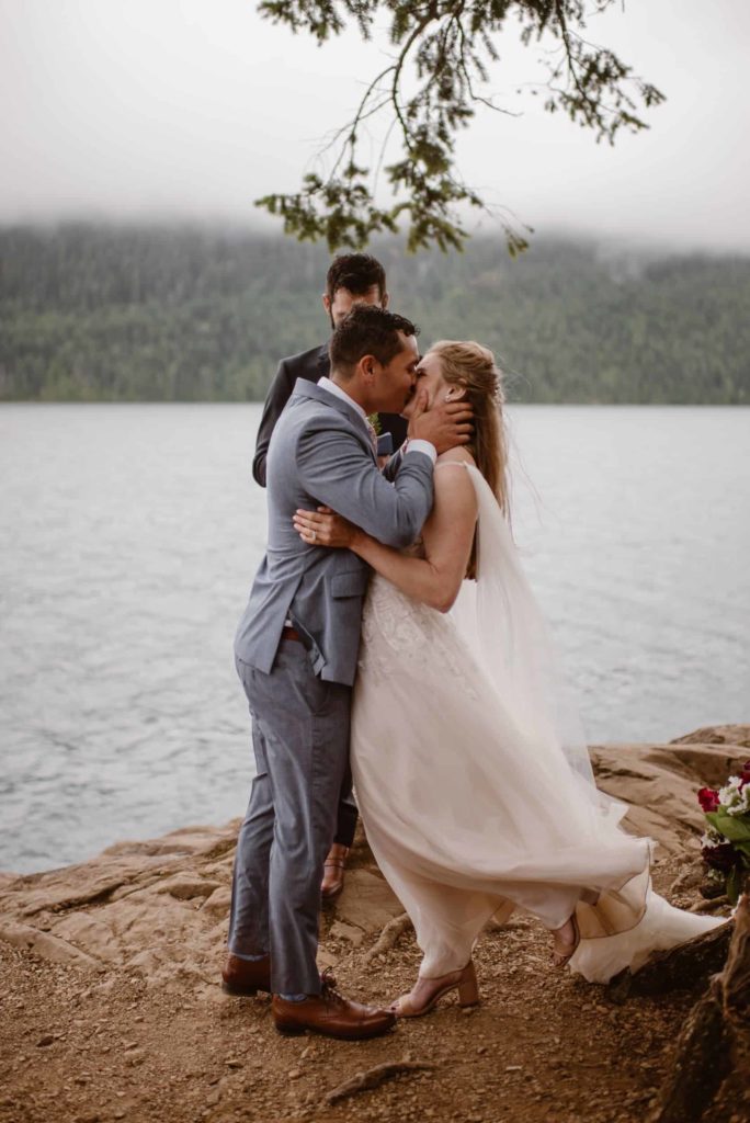 Bride and groom kiss in front of a lakeshore during their ceremony at Olympic National Park. 