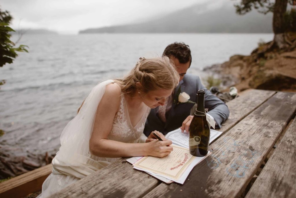 Bride and groom sign their marriage license on a picnic table in Olympic National Park. 