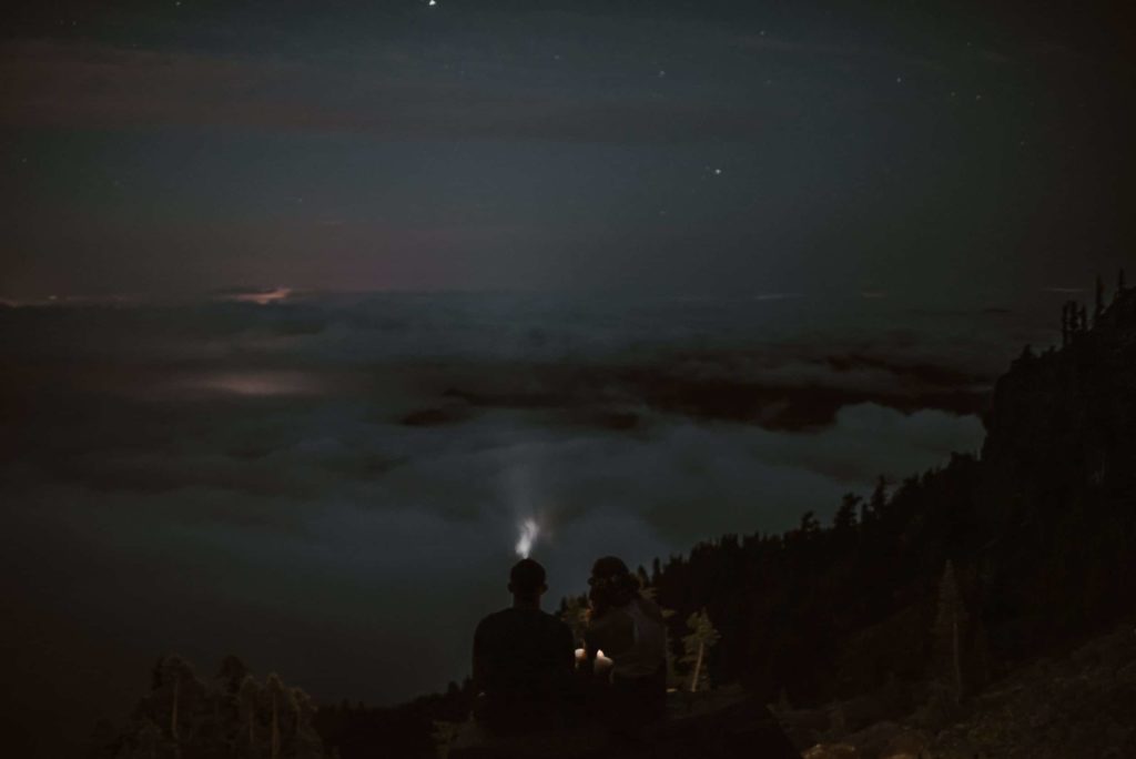 Bride and groom wear head lamps in the dark and overlook a think fog at Olympic National Park.