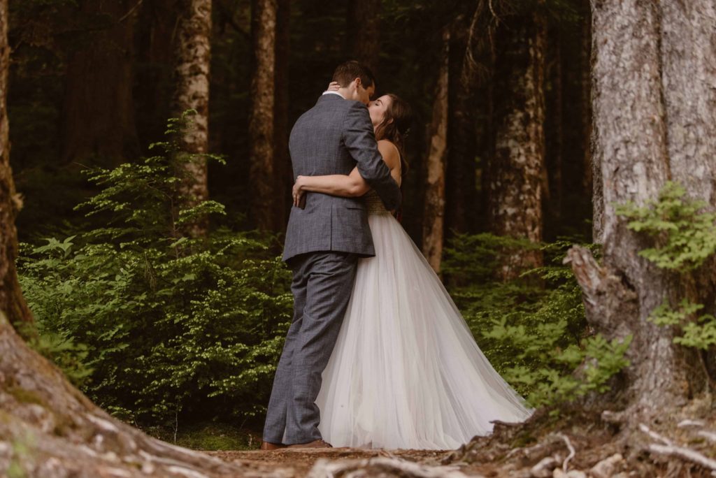Bride and groom kiss, surrounded by trees in Washington State Forest. 