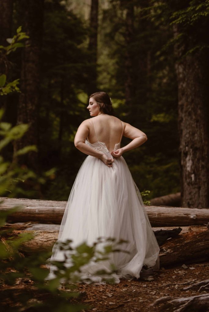 Bride zips up her dress in Washington State Forest. 