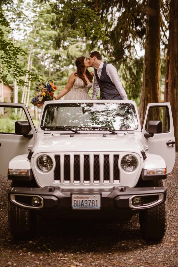 Bride and groom kiss while standing in a jeep.