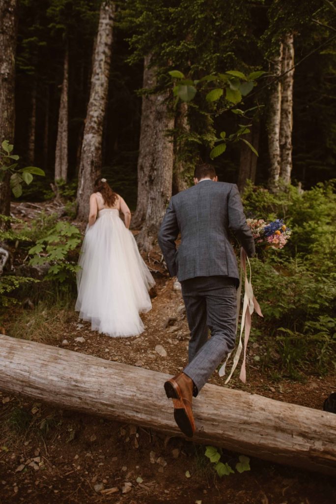 Bride and groom hike on trail into forest in Washington State Forest. 