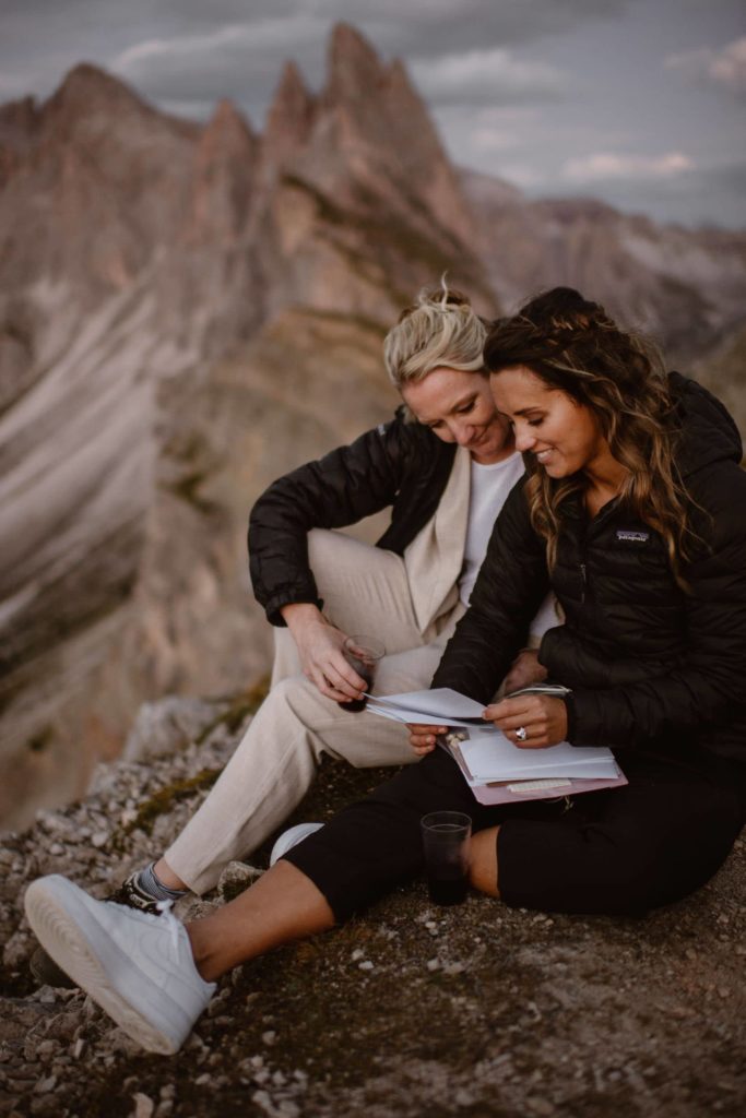 Two brides read letters from family and friends on top of the mountain.