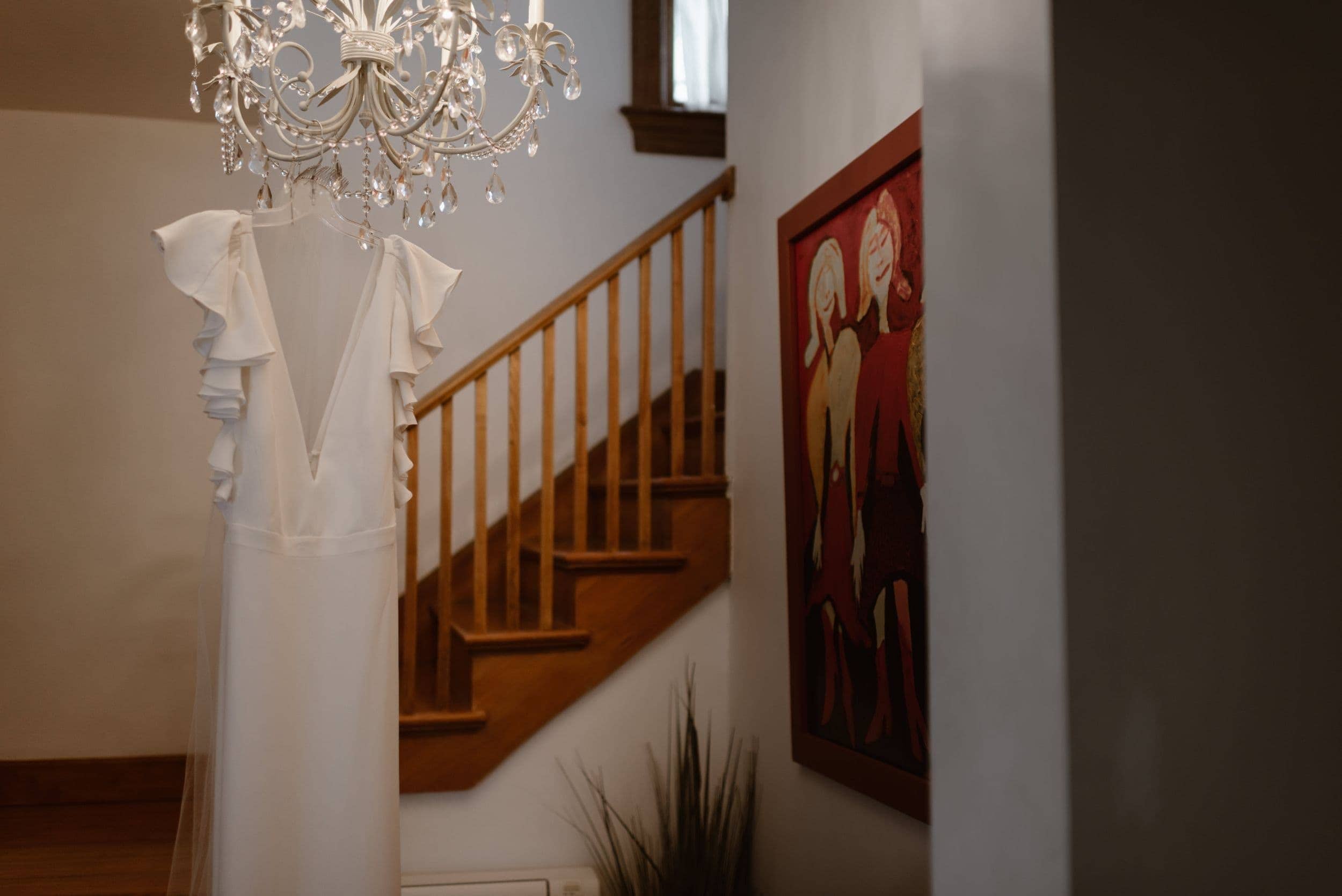 Bride's custom, white wedding dress hanging from a chandelier in Airbnb.