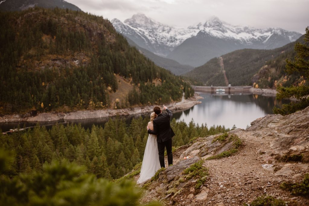 Bride and groom look off into the distance, while groom points at mountain range on Orcas Island. 