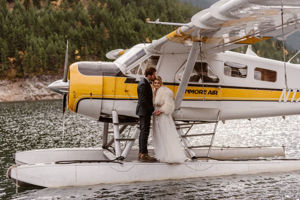 Groom kisses brides forehead while they stand on exterior of floatplane. 