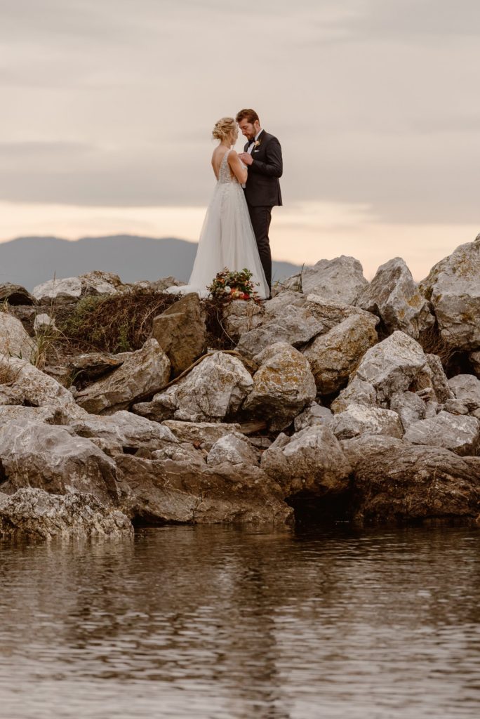 Bride and groom face each other and hold hands, while standing on rocks at Orcas Island. 