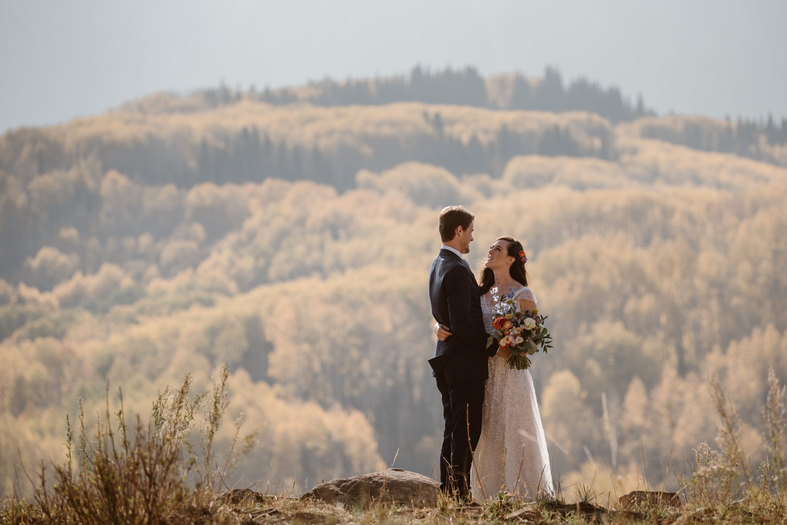 Bride and groom embrace, with forest and mountain in the background in Crested Butte, Colorado.