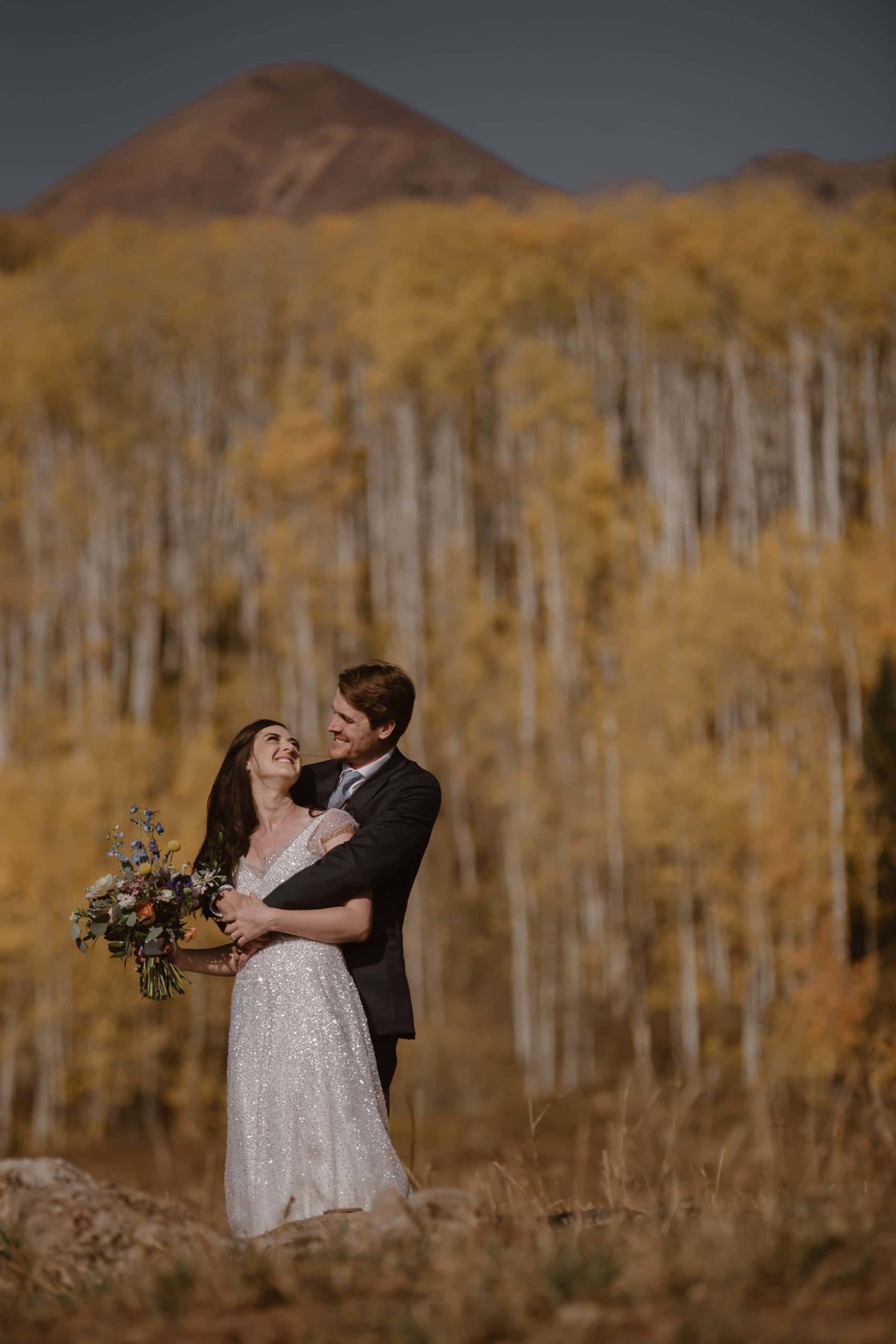 Bride and groom embrace while smiling at each other in Crested Butte, Colorado. There is an aspen grove in the background. 