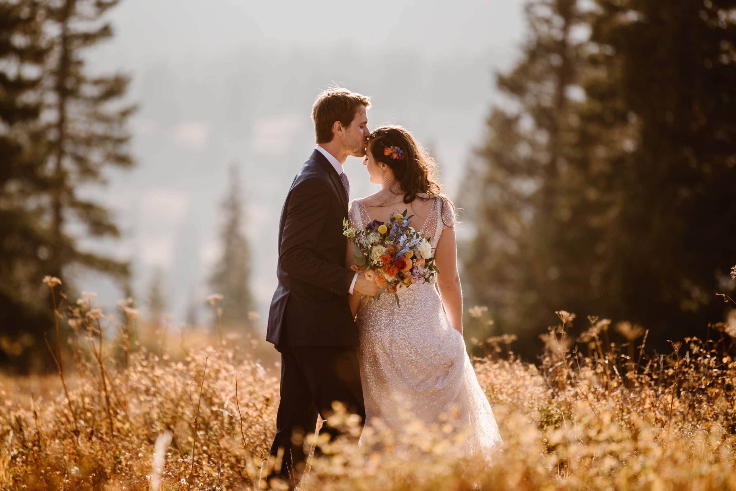 Groom kisses bride's forehead while they stand in a meadow in Crested Butte, Colorado. 