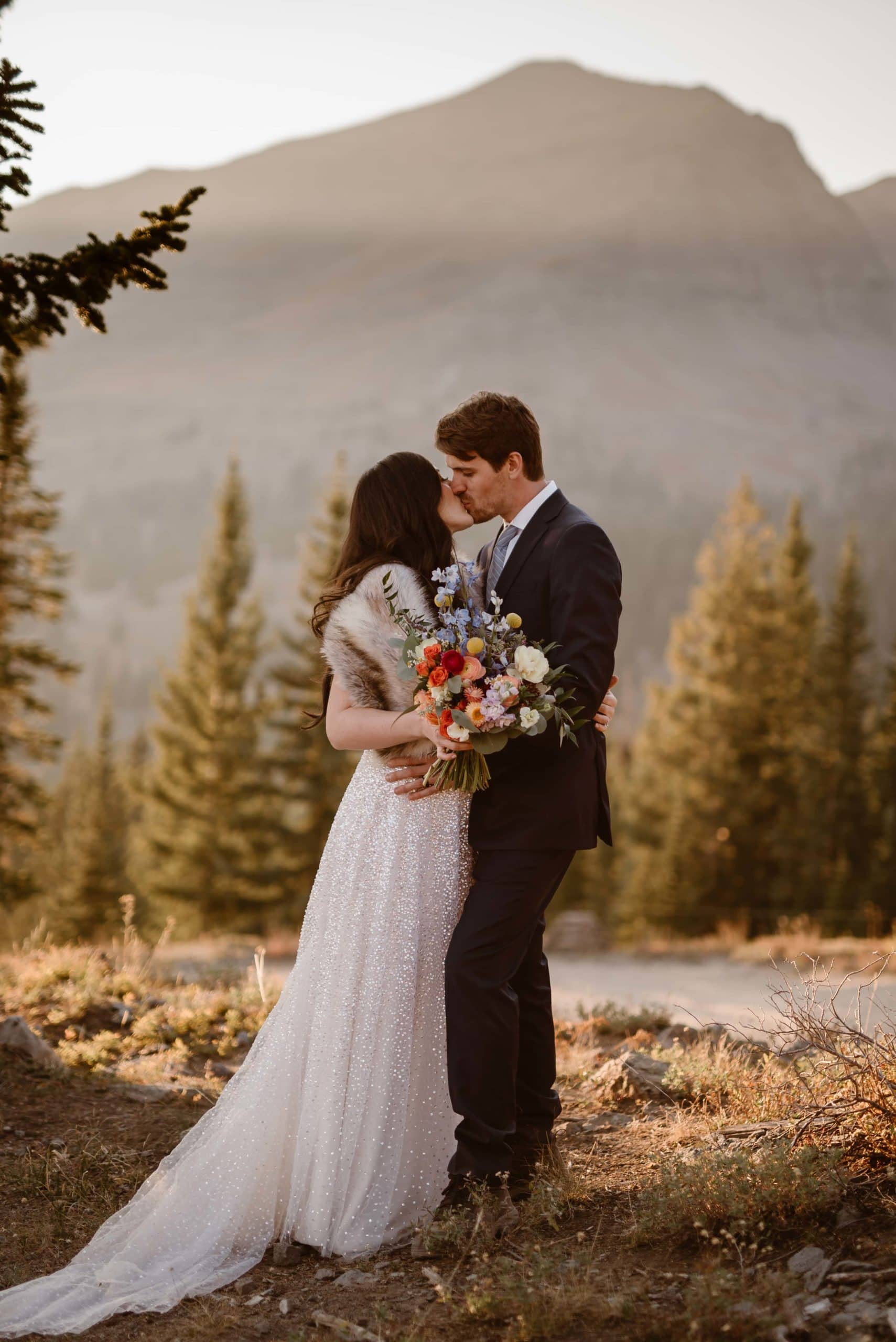 Bride and groom share a kiss on their elopement day in Crested Butte, Colorado. There are trees in the background. 