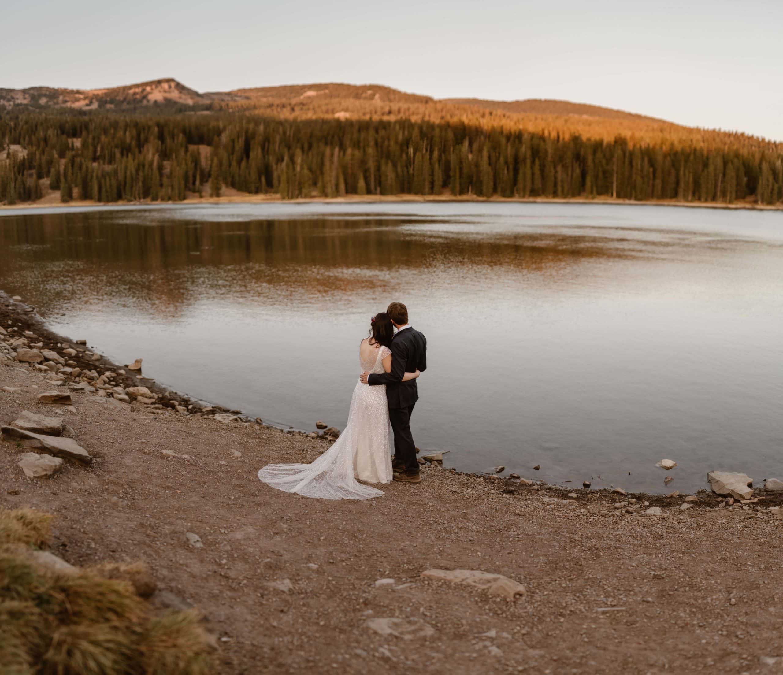 Bride and groom have their arms around each other while looking out at a lake and forest in Crested Butte, Colorado. 